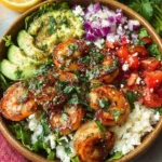 A vibrant Honey Harissa Shrimp Bowl topped with fresh herbs and vegetables.