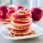 Peanut butter apple sandwiches topped with granola, a healthy snack option.