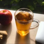 A cup of Korean Apple Tea with fresh apple slices and spices, showcasing its vibrant color.