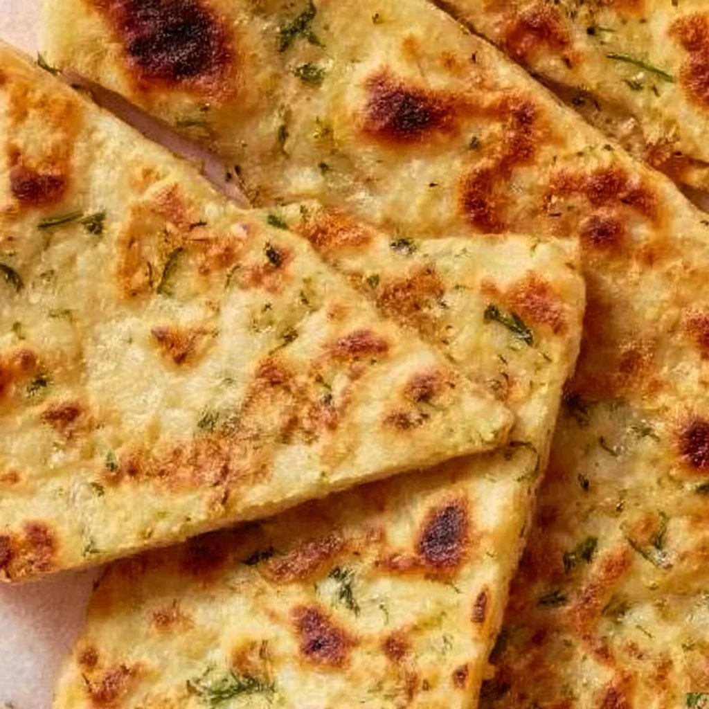 Soft potato flatbread topped with fresh herbs and vegan cheese on a wooden board.